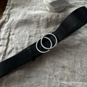 Svart Lindex Skärp - Svart skärp med silvrigt metallspänne i design av två cirklar. - Storlek S men har anpassats med 2 extra hål, så att den passar XS också.