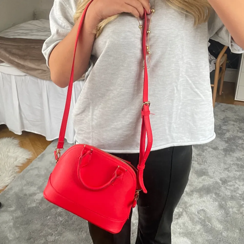 Röd väska i nyskick! Har både ett kort och långt band. Aldrig använd. Perfekt accessoar för att göra en tråkig outfit snyggare!. Väskor.