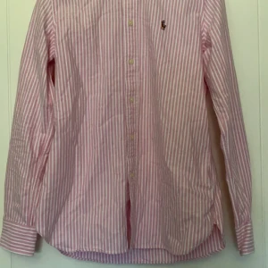 Ralph lauren skjorta - Fin Ralph lauren skjorta i färgen rosa med vita ränder. Perfekt plagg till sommaren och våren. Inga defekter eller liknande. Storlek S men passar förmodligen även XS. Tveka inte på att höra av er om ni har frågor!