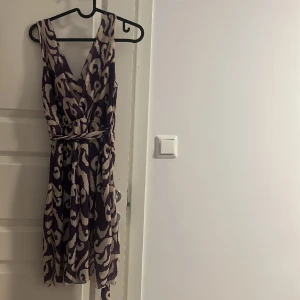 Beige och lila klänning - Passar storlek S. Det Finns två pyttesmå hål längst fram, annars i bra skick.