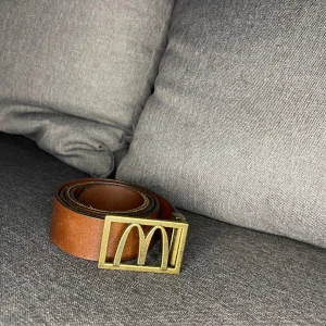 Mcdonald’s bälte - Storleken är justerad efter storlek 90. Men går att justera till mindre genom låset där det går att klippa av bältet för bästa passform. Skick: 4/5 (Använt men inget påtagligt slitage) Färg: Brun/guld