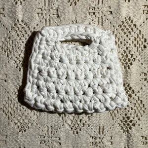 Vit Väska - Supersöt liten sommarväska, virkad i vitt tyg🤍18cm bred längst ner och 14,5cm högst upp, 16cm hög💕Är i gott skick bortsett från en liten missfärgning i tyget på baksidan, men syns inte när man använder den🤍