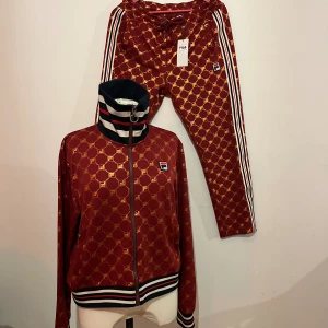 filaset - nyskick fila tracksuit i mörkröd med brons/guldiga detaljer, jackan är tvättad en gång och byxorna är oanvända💫
