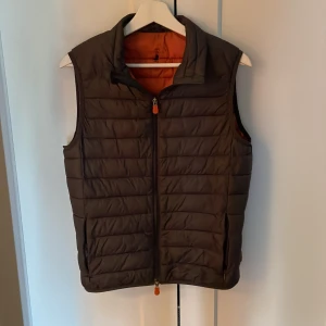 Save the duck väst - Grå Save the duck väst med orange insida. Västen är i bra skick och är i modellen ultra light jacket. Nypris ligger på 1 399 kr.