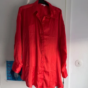 Lång orange och luftig skjorta - Lång, orange och glansig skjorta i svalt material. Lätt transparent.Längre baktill.