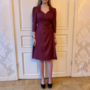 Plommon färgad omlott klänning, Emmy design  - Fin plommon färgad omlott klänning. Storlek 38 Knytet gör att den passar storlekar 36-40 Modellen på bilden är 173 cm och har storlek 38 i de flesta andra kläder. Aldrig använd. Vi har lagt ner vår klänningsbutik och säljer ut. Ny pris är 2000-3000kr