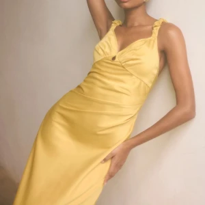 Adoore Satin Klänning - Nîmes Midi Dress in dusty yellow.  Köpt maj 2024 för 1 395 kr, använd 1 gång på bröllop, ren, ångstrykt.   The dress has a drop-shaped cut-out, a hook for adjustment at the bust and elastic scrunchie shoulder straps.