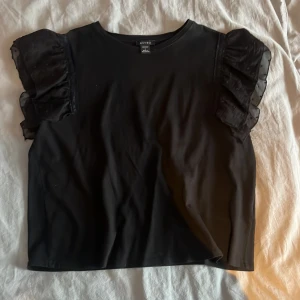 Svart volang t-shirt - Jättefin t-shirt med volang i armarna, köpt här på plick men knappt använd, strl L men passar mig som har S i vanliga fall💓 skriv för fler bilder 