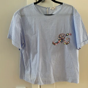 Blå och vit randig blus från Manoush i strl 42 i nyskick - Blusen har korta ärmar.  Mått Över axeln: ca 49 cm Längd från axeln och ner: ca 61 cm  Kommer från ett djur och rökfritt hem.