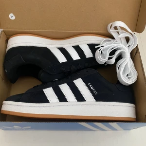 Nya Adidas Campus 00s -storlek 38 - Adidas Originals Campus 00 s j Storlek: 38 Färg: Svarta (Core Black / Cloud White / Cloud White) Ingår både vita och svarta skosnören.  Nya och oanvända. Ligger kvar i kartong. 
