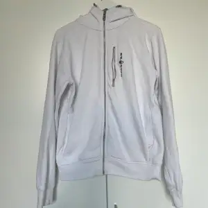 Säljer en vit sail racing zip hoodie. Är i bra skick förutom en liten fläck på ryggen (se bild 2) samt längst ner på högra ärmen. Storlek M.