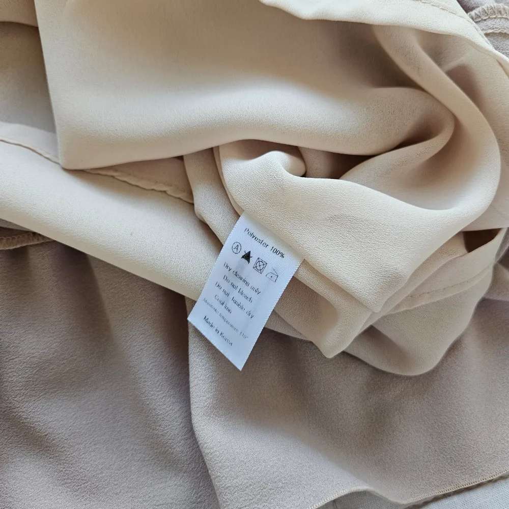 Kort, klockad modell med volang och knytning. Beige. Längd 85 cm. Storlek S/M. Mekot.