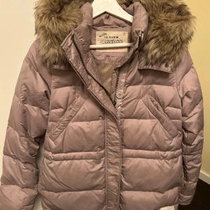 Odd Molly jacka - Oanvänd dunjacka från Odd Molly i storlek 0 (XS). Luva i fuskpäls som avtagbar. Dragsko i midjan för justera jackans form. 
