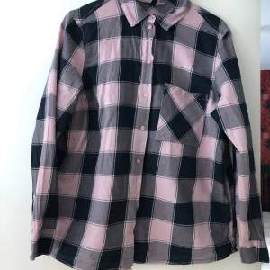 En rosa-svartrutig flanelliknande skjorta som passar att ha för sig själv, eller öppen över ett linne eller liknande. 💗