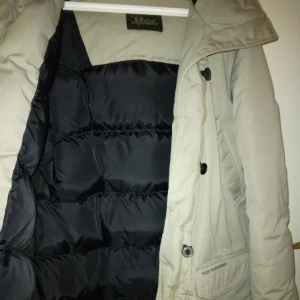 Beige äkta Peak Performance dunjacka/ dunparkas. Strk: Medium. Tjock & varm. - Äkta Peak Performance dunjacka/ dunparkas. Beige/gråbeige. Strk: Medium. Tjock & varm. Jackan stängs med dragkedja och knappar. Flera fickor - 4 st i fram samt 1 innerficka med dragkedja. Luvan går att rulla in. Bra skick, kan ev. behöva en tvätt.