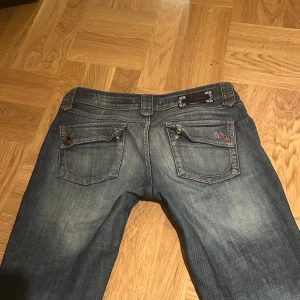 Bootcut jeans - Skit snygga bootcut jeans med röda detaljer som jag säljer då de inte kommer till användning. Lite slitningar i hälen (skriv för blir bilder) Midjemått: 43cm, Innerbenslängd: 77cm!! 💝
