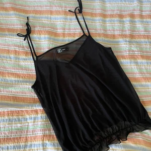 Svart linnetopp från Only - En svart mesh linne från Only med smala axelband och v-ringning. 