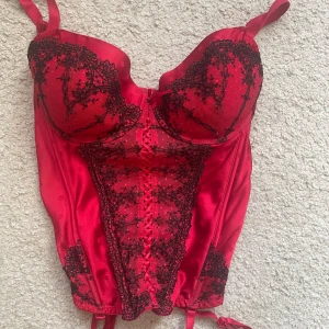 Röd/svart korsettopp - Så snygg korsettopp i röd och svart. Perfekt inför halloween eller annat. 85C kupa och justerbarband. Frakt ingår ej