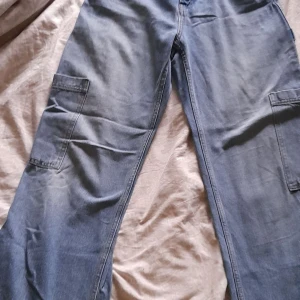 Blå cargobyxor - Ett par blå cargo jeans med flera fickor. Byxorna har en avslappnad passform och jag köpte de för 2 år sedan, så de är lite använda. Storlek 36. 