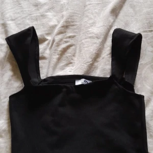 Svart topp från Carla Mara - En svart topp från Carla Mara med breda axelband. Toppen är ärmlös och har en enkel design. 