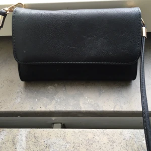  - Snygg och enkel liten axelväska/aftonväska med inbyggd plånbok. Kan även användas som clutch då axelremmen är avtagbar.

Väskan är i extremt gott skick, endast använd en gång på kompisars bröllop förra året. Jag har inget behov av väskan och säljer den därför till någon som vill slippa släpa med sig en stor väska ut. 

Två fack för mobil eller nycklar + ett fack med dragkedja. 7 rymliga kortfack + fack för sedlar/mynt med dragkedja. Material i svart fejkskinn. Axelremmen har guldiga detaljer.

Höjd: 11 cm
Bredd: 18,5 cm
Tjocklek utan innehåll 3 cm

Axelremmen är 130 cm (OBS avtagbar)

Jag kan frakta för 30 kr eller mötas upp i Stockholm. 

Tar betalt via swisch, Plick, kontoinbetalning eller kontant.

