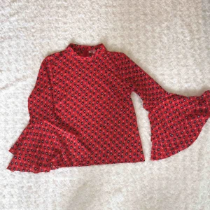  - Mönstrad blus med trumpetärmar från Indiska. Hög hals med diskret dragkedja i ryggen (går att se på bild 2). 98% polyester och 2% elastan.  Kan mötas upp alt. skicka.