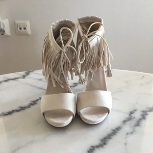  - Ett par beige klackar med fransar högst upp! Aldrig använda! Man knyter dom fram! Köparen står för frakt på 90kr 