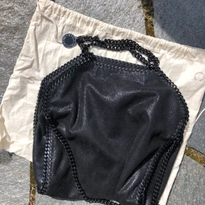 Stella McCartney väs (svart, falabella) - Säljer nu min fina svarta Falabella bag som endast är använd ett fåtal gånger. Säljes i nyskick och köpt på Stella McCartney i Stockholm. Pris: 3000 kr exklusive frakt. Bredd 38 cm och höjd 37 cm. 