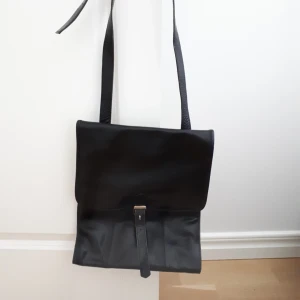  - Svart läderväska med justerbart axelband. Remmen vid spännet är lite sliten annars i fint skick. Ett stort fack samt ett litet innefack. 