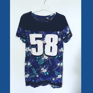 Blå/lila Klänning från H&M- Strl 44 - Blålila klänning med tropiskt mönster och print från H&M i storlek 44 (oversized). Endast använd ett fåtal gånger och så gott som ny. Kortärmad och med tunnare tyg längst nyckelbenen. Slutar strax över knäna.