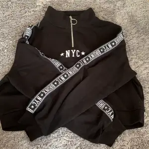 A black cropped Jodie with NYC * BRONX written on the sleeves. It has a zipper at the top that goes from the neck till between the boobs