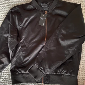 Oanvänd bomberjacka - Helt oanvänd bomberjacka från Lager 157. Tunn så skulle säga vår-/sommarkväll-jacka. Glansig finish med roseguldiga detaljer. Superfin men använder inte guld. Priset går att diskutera!! Köparen står för frakten. 