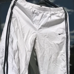 NIKE Joggers - Skitsnygga Nike byxor i tunt skjortmaterial. Byxorna har fickor med dragkedja, och en jättefin detalj nere vid foten där det går att öppna och göra byxan vidare.