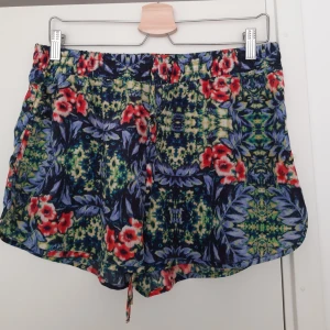 Shorts i blommig detalj  - Shorts med tropisk/blommig detalj. Köparen står för frakt alt hämtas i Uppsala.