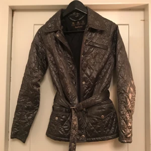  - Grå glansig jacka från barbour med bälte i midjan i klassisk modell. Jackan är ljusare grå i verkligheten. Nyskick.  *Frakt ingår i priset👍🏼*