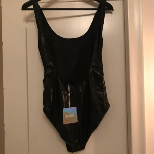  - Body i glansigt fakeskinnmaterial med urringad rygg. Helt ny med lappar. *Frakt ingår i priset👍🏼*