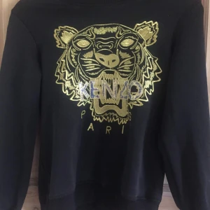  - Svart fake Kenzo långärmad tröja med guldiga detaljer. Använd men fortfarande i gott skick. Säljer åt min syster så all information jag har om plagget får jag av henne! Frakt blir 56 kr :) 