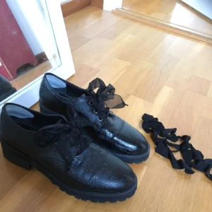  - Glansiga skor med en låg klack och tjock sula. Två par snören - sidenband och vanliga svarta. 👢👠 Tillverkade i skinnimitation och kommer från Monki. Pyttelite slitna på insidan, vilket kan ses på bild tre. 