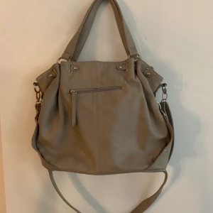 Handväska - Superfin och rymlig handväska. Den är använd (dragkedjan har tappat en del men fungerar) 2-3 innerfickor/fack. Ett justerbart axelband och två ”handtag” att bära den i. Köparen står för frakten. Fraktar endast.