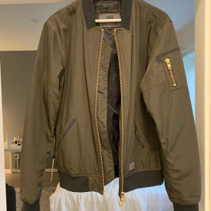 Brixton bomberjacka  - Mörkgrön Brixton bomberjacka med svarta och guldiga detaljer. Jackan är i nyskick. Sparsamt använd. Nypris cirka: 1300:-