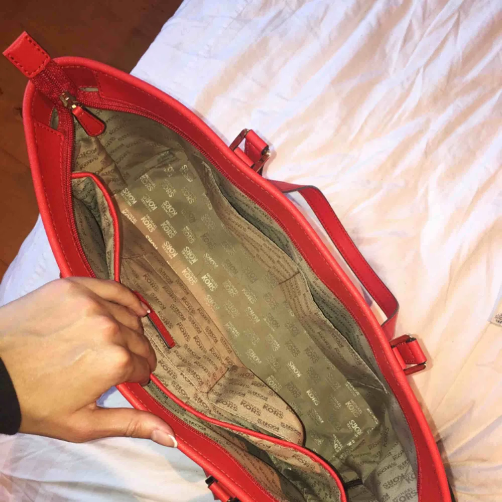 Michael Kors-väska i röd färg med guld detaljer. Köpt i New York för 4700kr, knappt använd. Har 4 mindre fack samt ett större fack innanför samt ett fack på baksidan utanför. Den kan stängas med dragkedja. :). Väskor.