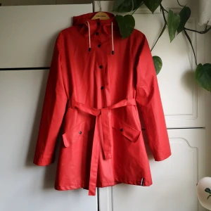 Marin Alpin Sportswear - Regnjacka med skärp - Klarröd regnjacka i galon från Marin Alpin Sportswear. Lätt fodrad. Använd men gott skick. 
