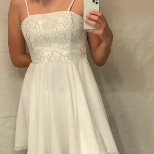 Vit cocktailklänning  - Cocktailklänning från Swing. Slutar ovanför knäna. Endast använd en gång så i väldigt bra skick & kvalitet. Köpt för omkring 1000 kronor. 