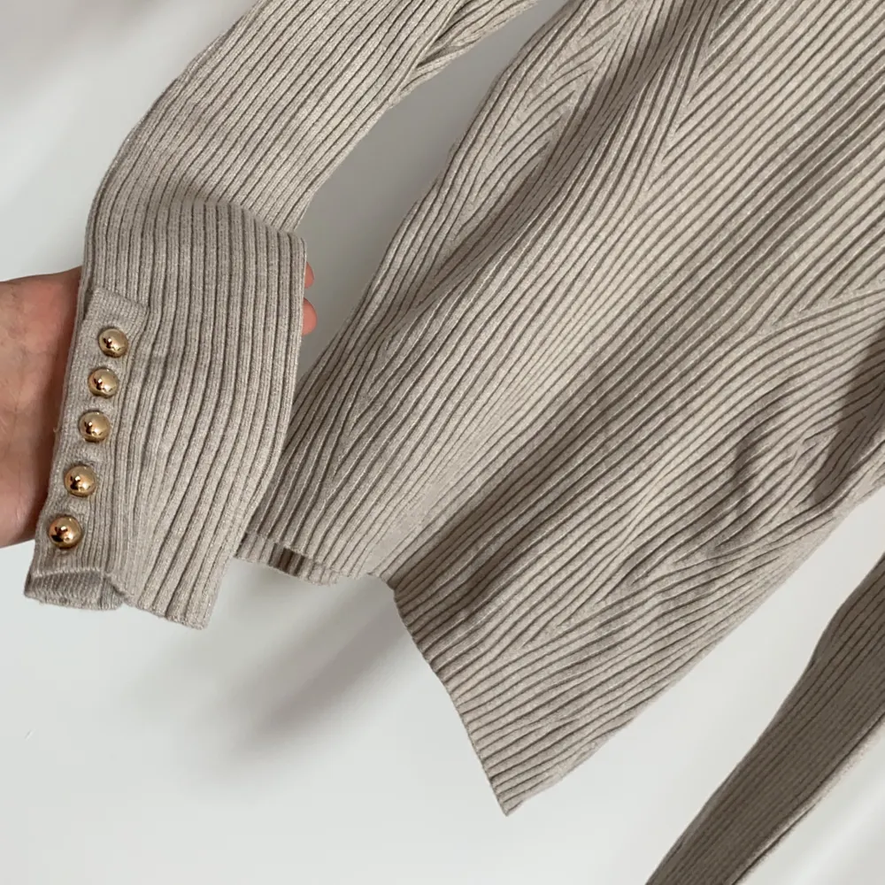 Beige ribbstickad polotröja i stretchigt material med knappar längst ut på ärmarna. Nyskick!. Stickat.