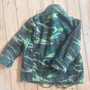  - Camouflage-jacka i strl S, passar även M, vilket jag vanligtvis har.  Kort modell med trekvartsärm, snygga detaljer. Stängs med dragkedja samt knappar.  Färgen stämmer bäst överrens med bild 2.  Inköp secondhand i New York. Bra skick.