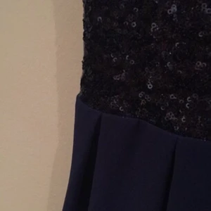  - Mörkblå klänning med glittrigt överparti. Använd ett fåtal gånger. Insydd lite i sidan samt i u-ringningen på ett snyggt sätt. V-ringning med dragkedja bak. Pris exklusive frakt.  