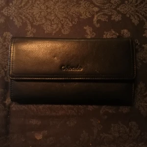 Plånbok i läder - Colorado står på framsidan. Ficka finns på baksidan och ett flertal i innersidan. Utrymme för fler kort och kontanter finns. 