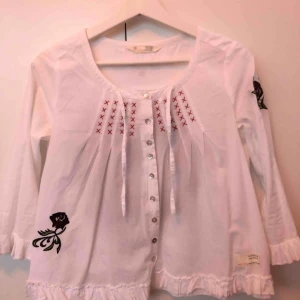 - Söt, vit Odd Molly blus med många detaljer. Broderier på både fram- och baksida samt ärmar och knappar framtill. Ärmarna är trekvarts och har volanger i slutet. 