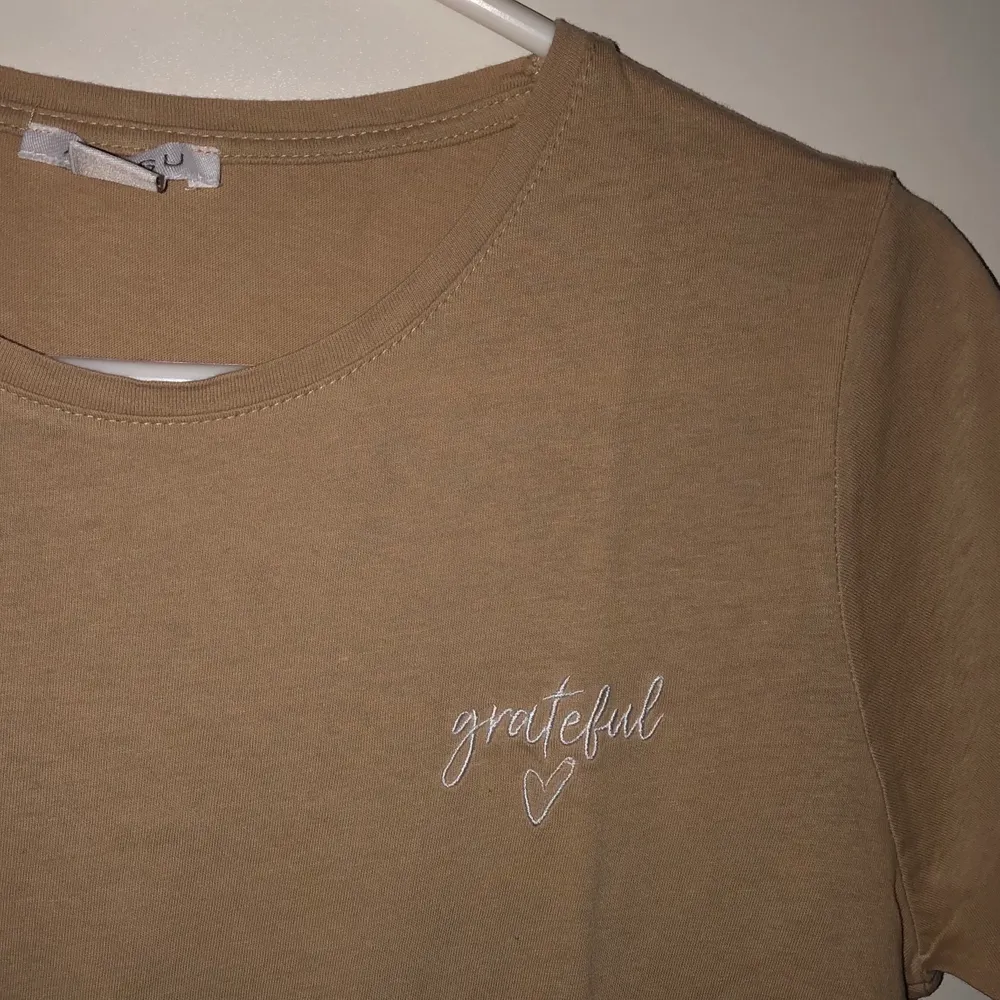 Beige t-shirt i nyskick. Aldrig använd. Texten ”grateful” på bröstet. Frakt är inkluderat i priset.. T-shirts.
