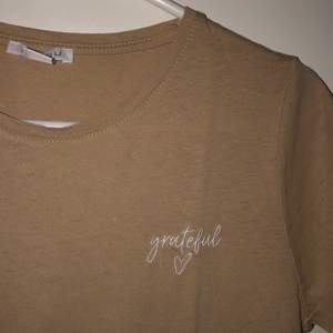 Beige t-shirt i nyskick. Aldrig använd. Texten ”grateful” på bröstet. Frakt är inkluderat i priset.